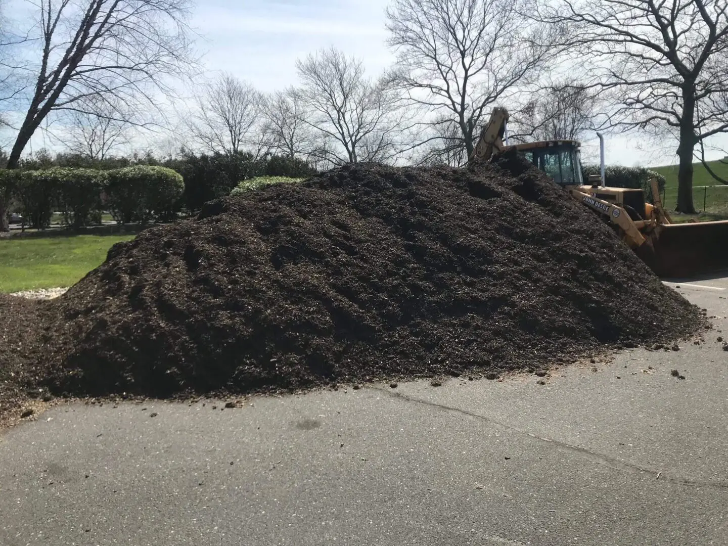 A large pile of dark soil or mulch outdoors on pavement.