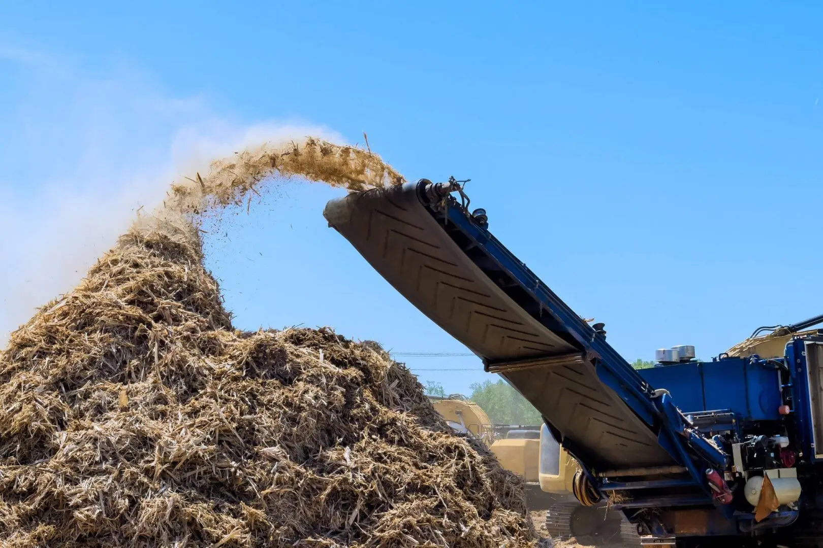 Machine processing mulch or wood chips against blue sky.