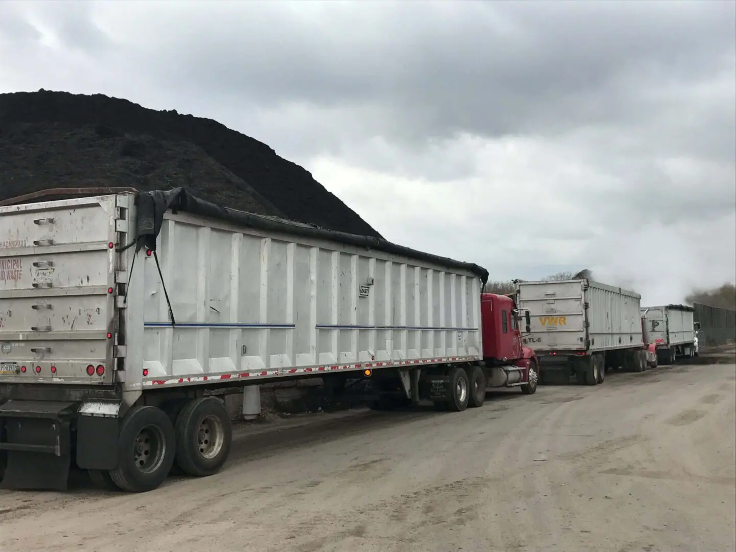 Two large trucks loaded with coal parked under a cloudy sky.