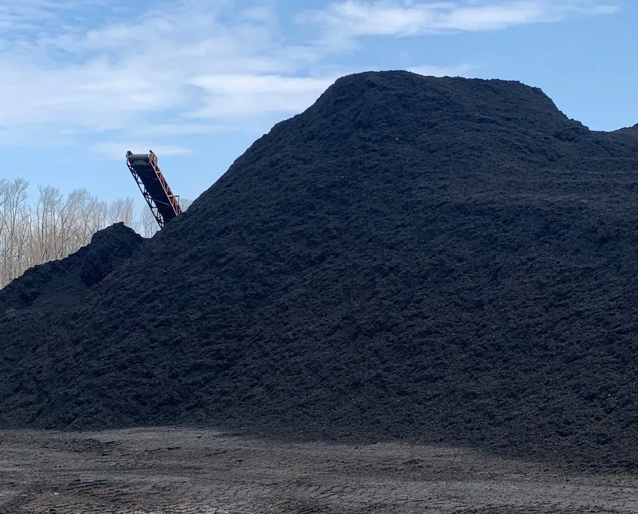 Large pile of black mulch under sky.