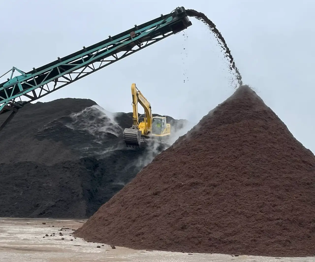 Excavator stacking a large pile of soil with a conveyor belt.