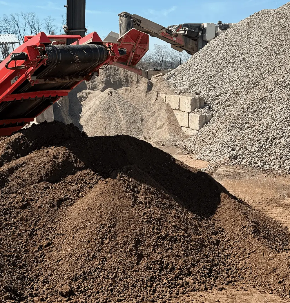Pile of soil and gravel at a construction site with machinery in action.